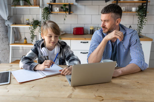 istock Father helping his teenage son with homework while working from home in the kitchen. Concept of parenthood, fatherhood, spending quality time together. Using technology, gadgets, devices for learning 1399784136