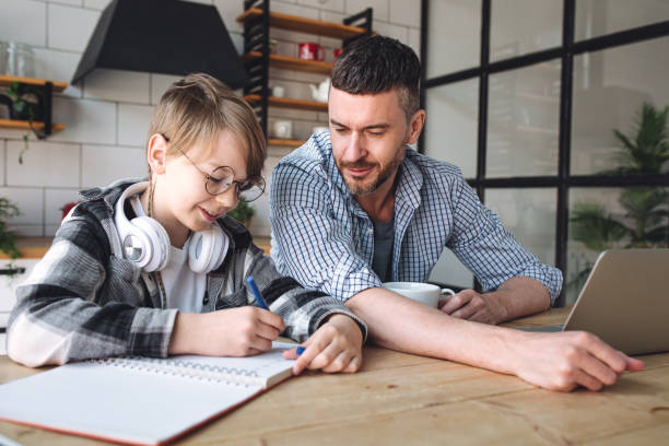 istock Father helping his teenage son with homework while working from home in the kitchen. Concept of parenthood, fatherhood, spending quality time together. Using technology, gadgets, devices for learning 1399785420
