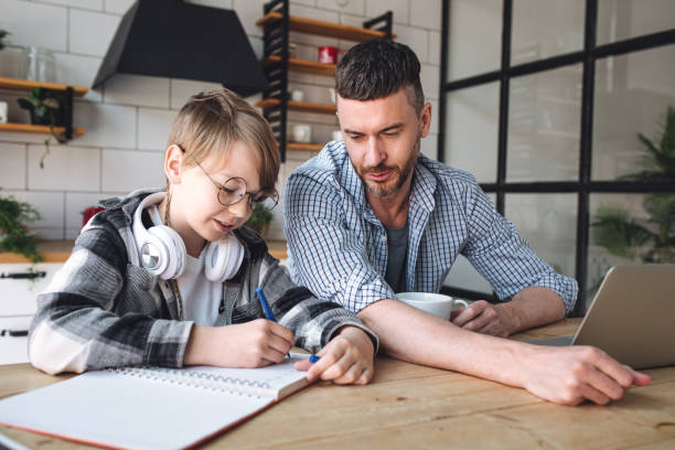 istock Father helping his teenage son with homework while working from home in the kitchen. Concept of parenthood, fatherhood, spending quality time together. Using technology, gadgets, devices for learning 1399785581