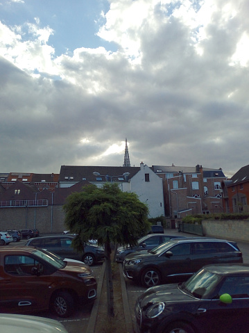 Leuven, Vlaams-Brabant, Belgium - May 28, 2022: white sky above the top of the cathedral. It seems as God is illuminating and shining on this religious building. Front parking cars at shopping supermarket Colruyt Leuven