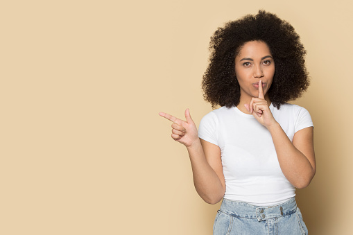 Happy millennial African American woman isolated on yellow background point at blank empty copy space. Smiling young biracial female show good sale offer or promotion deal. Copyspace, ad concept.
