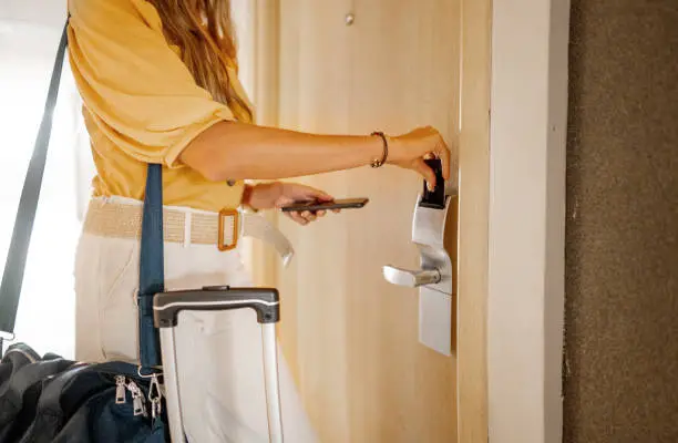 Close-up of a businesswoman with a bag using a keycard to open her room door after arriving at a hotel during a business trip