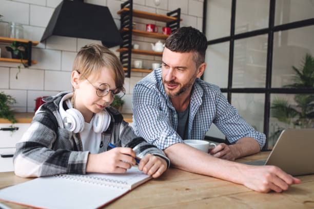 istock Father helping his teenage son with homework while working from home in the kitchen. Concept of parenthood, fatherhood, spending quality time together. Using technology, gadgets, devices for learning 1399787899