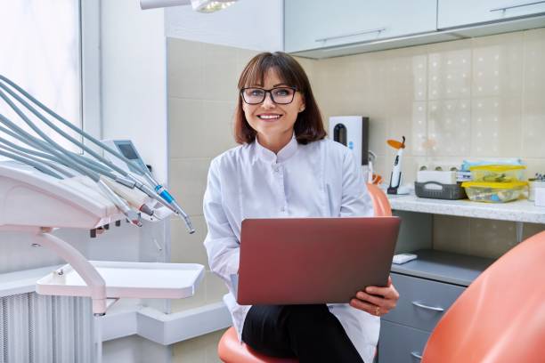 Portrait of doctor sitting in office with laptop in her hands looking at camera stock photo