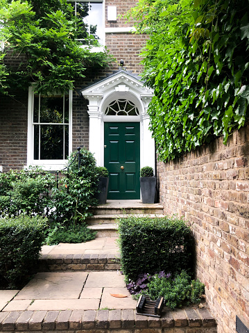 Facade of the residential house in Chelsea, London covered in vivid greenery, with a brightly-coloured door.