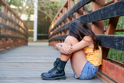 Teen girl sitting on bridge with head down