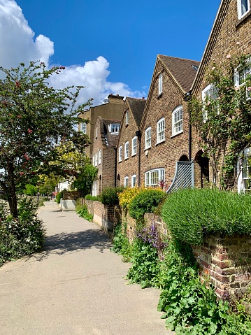 Street view of Strand on the Green riverside. Fragment of dutch and english facades with brick wall and front garden with bushes and flowers. Chiswick