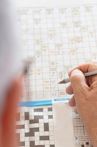 Over the shoulder view of a senior man wearing eyeglasses doing crossword puzzle.