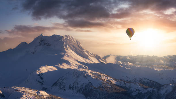 Dramatic Mountain Landscape covered in clouds and Hot Air Balloon Flying. 3d Rendering Adventure Dream Concept Artwork. Aerial Image from British Columbia, Canada. Sunset or Sunrise Sky