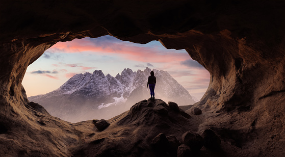 Dramatic Adventurous Scene with Woman standing inside a Rocky Cave Landscape. 3d Rendering. Sunset Sky. Mountain Image from Alaska, USA. Adventure Concept