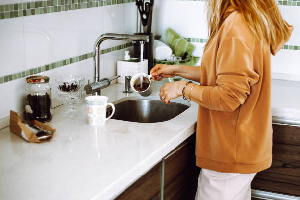 photo recadrée d’une jeune femme aux cheveux blonds ondulés portant un sweat-shirt brun, lavant la tasse de café sous l’eau libre. - sweat women wet shirt photos et images de collection