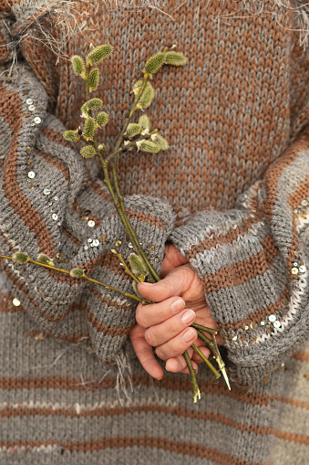 Foto recortada de una mujer sosteniendo un ramo de ramitas de sauce con flores verdes y esponjosas de amentos en las manos detrás de la espalda. photo