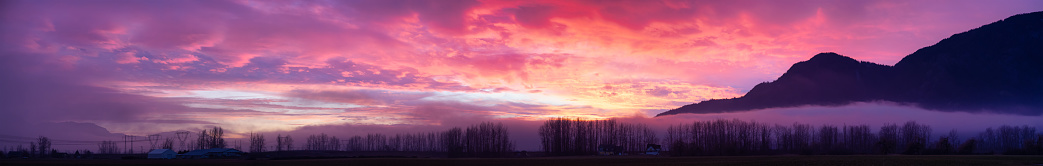 Panoramic View of Farm lands and Canadian Mountain Nature Landscape. Dramatic Winter Sunset. Located near Chilliwack and Abbotsford, British Columbia, Canada.