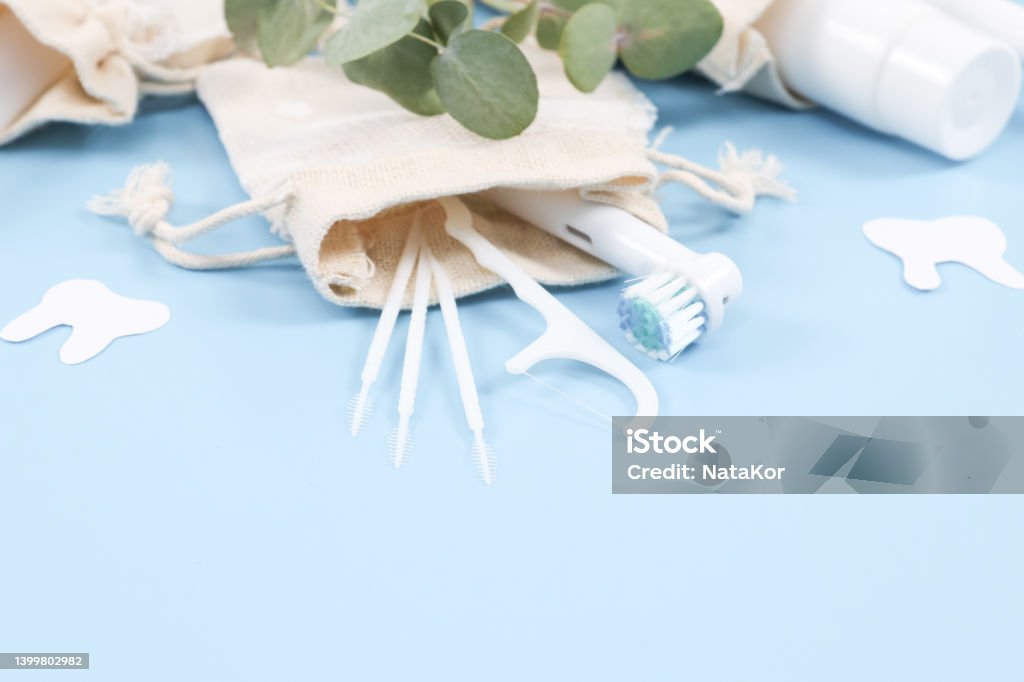 A set of toothbrushes, toothpicks, dental floss and toothpaste in cotton bags on soft blue. Set of toothbrushes, toothpicks, dental floss and toothpaste in cotton bags on a gentle blue background, close-up side view. Bag Stock Photo