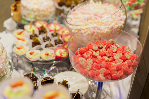 Colorful Candies in jars on a dessert table with donuts, cookies, and popcorn. There are cute chalkboard signs.