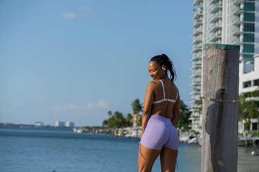Afro-Latin woman of average age in her 30s dressed in sportswear is outdoors near the beach doing physical exercises to get fit