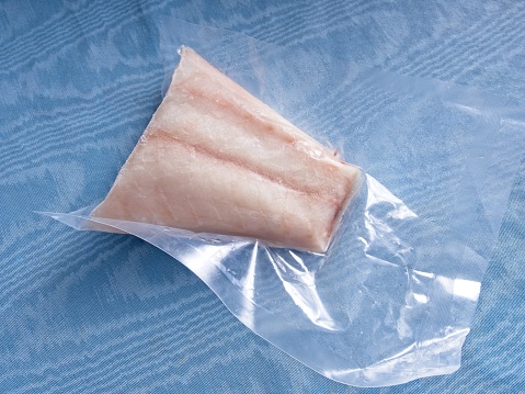 Frozen Red Snapper fish still in the protective plastic, a warm water white fish. Fish on blue table background.