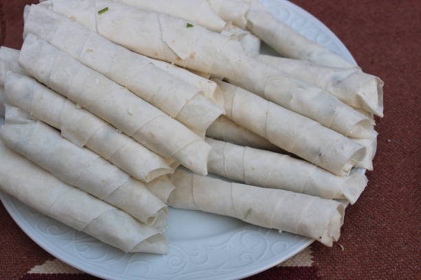 istock Raw Turkish cigarette shaped rolls and stuffed with cheese, purslane, dill or parsley. Cigarette shaped rolls on white plate. Selective focus. 1399808003