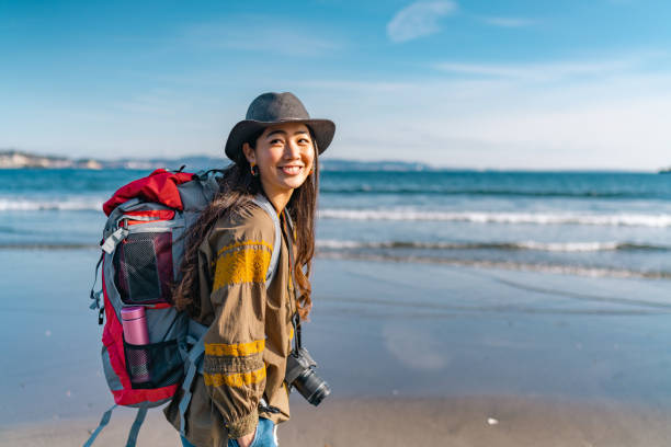 junge weibliche reisende, die in ihrem urlaub gerne zeit am strand verbringt - backpacker green vacations outdoors stock-fotos und bilder