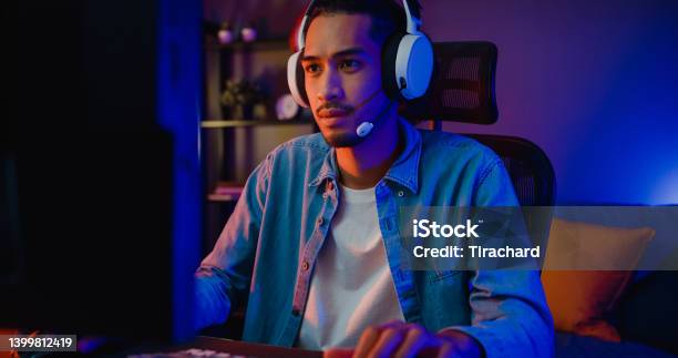Happy Asia Guy Gamer Wear Headphone Participation Play Video Game Colorful Neon Lights Computer In Living Room At Night Modern House Stock Photo - Download Image Now