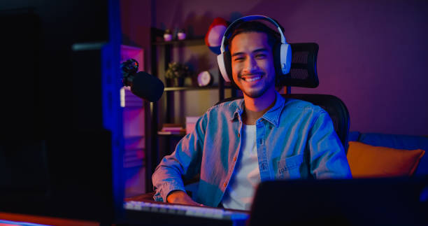 happy asia guy gamer wear headphone participação em videogame vídeo-jogo colorido neon lights computador e olhar sorridente para a câmera na sala de estar na casa moderna noite. - serpentina - fotografias e filmes do acervo