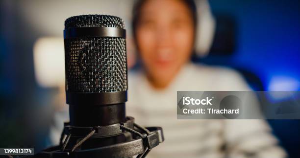 Happy Asia Lady Blogger Music Influencer Record A Podcast On Computer With Headphones And Microphone Talk With Audience In Living Room Home Studio At Night Stock Photo - Download Image Now