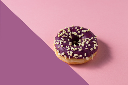 Donut with blueberry glaze and nuts  on two colour background .Sweet minimalist food image. Modern concept.