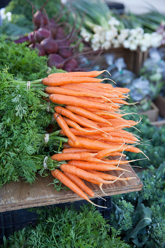 Bunches of freshly-picked orange carrots on display at a farmer's market.  Other vegetables, including beets and green onions, can be seen behind the carrots.