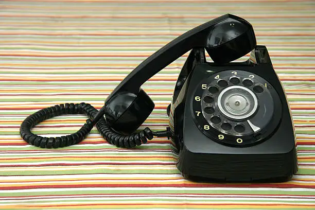 Old black telephone on multicolored striped table-cloth