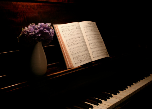 purple hydrangea flowers in vase and hymnal open on music stand of old upright piano