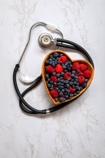 This is an overhead photo of a heart bowl of berries on a white marble background