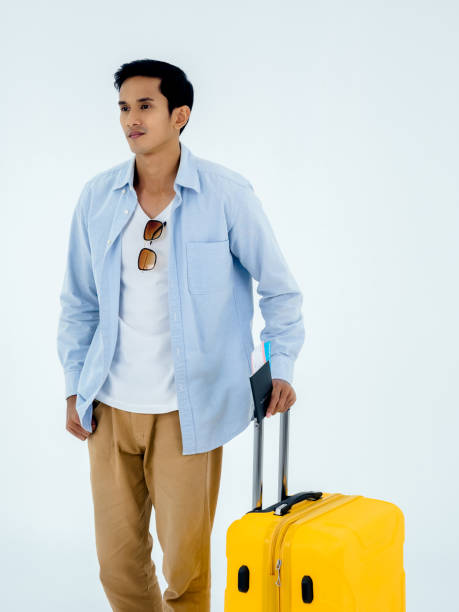 istock Ready to trip. Passport with flight ticket in young Asian man's hand while walking and holding yellow suitcase handle isolated on white background, vertical style. Summer vacation, holiday, tourist. 1399838469