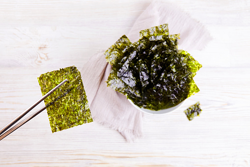 Chopsticks with a piece of crispy dried seaweed. Nori, Japanese edible seaweed in a plate. A healthy snack.