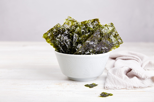 Crispy nori seaweed on bowl on grey background. Traditional Japanese dry seaweed sheets. Healthy snack.