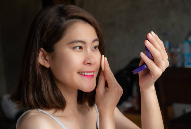 happiness asian woman applying foundation powder puff on her face to cover flaws and change the natural skin tone. - powder puff imagens e fotografias de stock