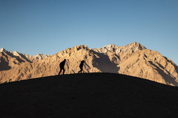 The two men’s walking on the sand dune at the mountains background at the sunset