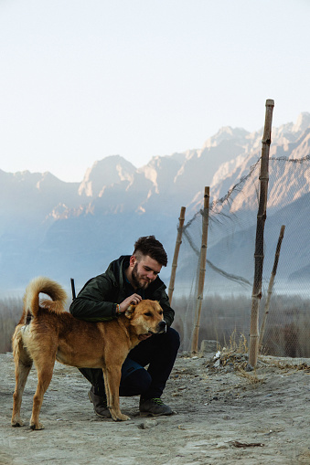 A man stroking a dog in Cold Katpana Desert among Karakoram mountains in Pakistan