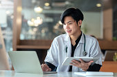 istock Asian male internship doctor sitting using laptop computer in the office. 1399844477