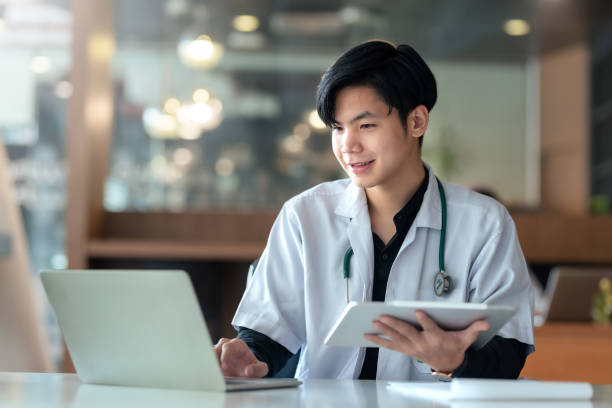 Asian male internship doctor sitting using laptop computer in the office. stock photo