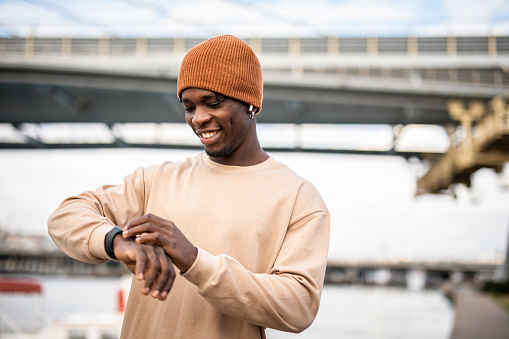 A young black man, an athlete, looks at his smartwatch and controls information after his training