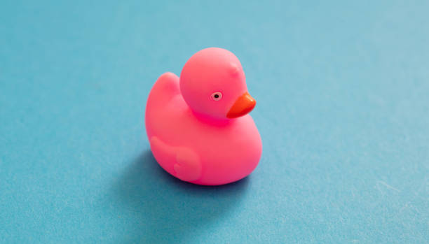 istock Pink plastic duck isolated on blue background. Baby bath fun toy. Overhead view. 1399846345