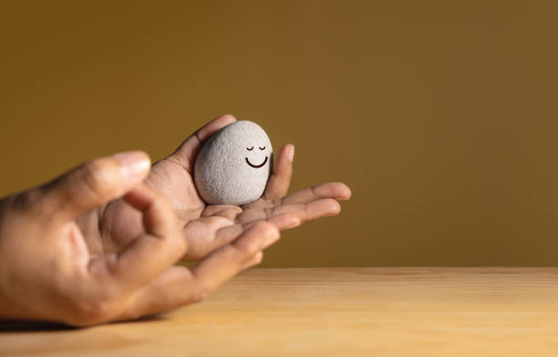 lebensfreude konzept. harmonie und positiver geist. sich gedanken über das ausbalancieren machen. nahaufnahme einer person, die hand für die meditation mit einem lächelnden kieselstein macht. geistige gesundheit - stone stability balance zen like stock-fotos und bilder