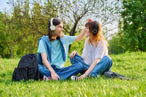 友人のカップル 17歳、18歳の男の子と女の子 芝生の上に座っている - 18 19 years audio ストックフォトと画像