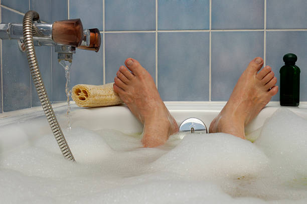 Soaking in a  Nice Hot Bath A man's feet, poking out of a bubble bath, with water running in to the side. A loofah and bottle of bath lotion to either side. Space for text on the blue tiled wall above the feet. heat home interior comfortable human foot stock pictures, royalty-free photos & images