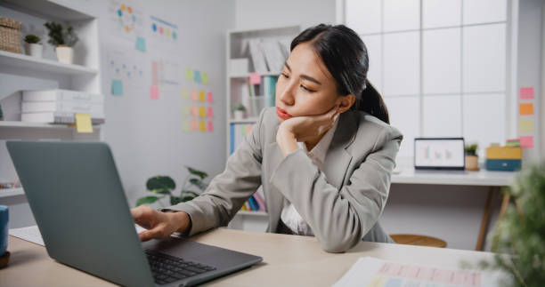 Young Asian businesswoman sit on desk with laptop overworked tired burnout syndrome at office. stock photo