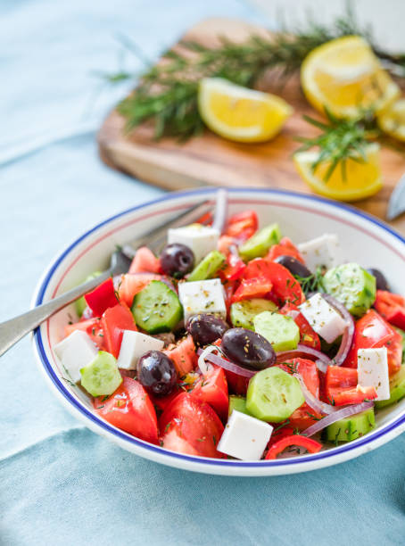 Greek salad with feta cheese, olives, tomato, cucumber and red onion, healthy vegeterian mediterranean diet food, low calories eating. Blue fabric background, top view stock photo