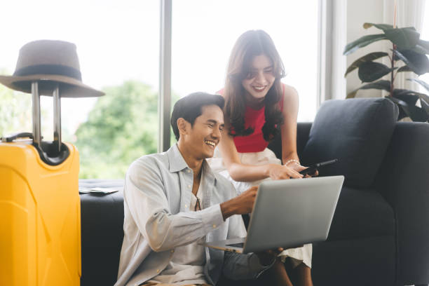 szczęśliwy uśmiech młoda dorosła para z azji południowo-wschodniej korzystająca z laptopa do przygotowania się do podróży na wakacje - southeast asian ethnicity men laptop image type zdjęcia i obrazy z banku zdjęć