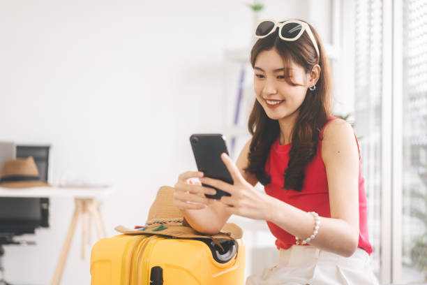 портрет молодой взрослой женщины из юго-восточной азии, использующей смартфон для покупки билета на самолет или онлайн-регистрации дома - airplane smart phone travel mobile phone стоковые фото и изображения