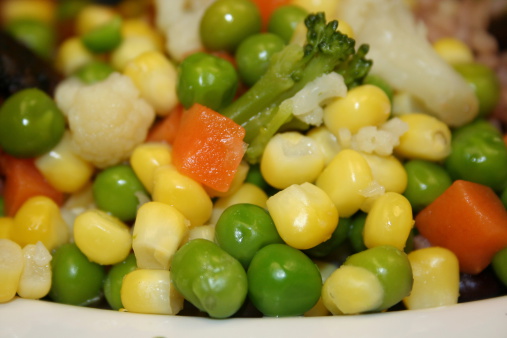 Close up of mixed cooked vegetables on a white plate. Vegetables include sweetcorn, peas, carrots, broccoli and cauliflower.