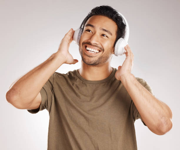 istock Handsome young mixed race man listening to music while standing in studio isolated against a grey background. Hispanic male streaming his favourite playlist online using wireless headphones 1399862938